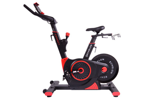 Black and red stationary exercise bike with digital display, adjustable handlebars, and foot pedals on white background