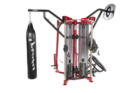 Red and black Hoist MCS-8005 multi-station gym equipment with boxing heavy bag attachment on left arm, displayed on white bac