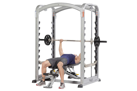 Silver and black dual action Smith machine with adjustable weight pegs, curved top frame, and footrest on white background