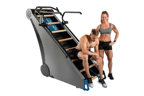 Jacobs Ladder X climbing machine with gray body, black and yellow steps, blue base, and handrails on white background