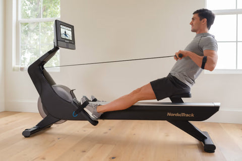 Black NordicTrack RW700 rowing machine with articulating touchscreen display showing workout video, flat lay on white backgro