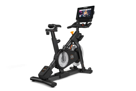 Black NordicTrack S15i indoor exercise bike with attached touchscreen display showing workout content, viewed from side on wh