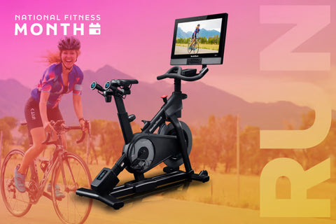 Black indoor stationary exercise bike with touchscreen display console mounted on adjustable arm, shown on white background