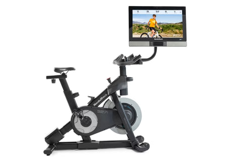 Black and silver NordicTrack S27i stationary exercise bike with attached tablet display showing cycling workout video, on whi