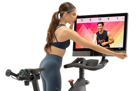 Black and silver NordicTrack S27i stationary exercise bike with attached tablet display showing cycling workout video, on whi