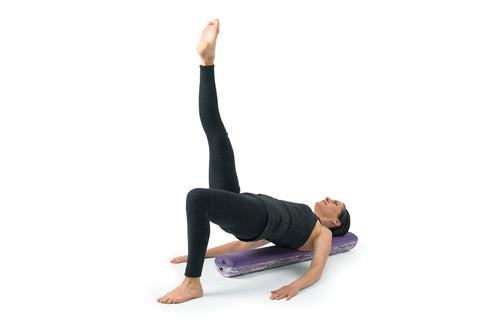 Woman lying on purple convex foam roller demonstrating abdominal exercise, wearing burgundy tank and black capris