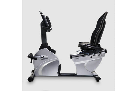 TRUE ES700 recumbent exercise bike with white and black frame, mesh backrest, and digital console on gray background