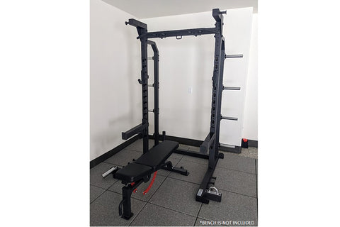 Black power rack with dual squat stations, weight plate storage on both sides, barbell, and adjustable bench on white backgro