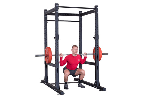 Black power rack with adjustable weight bar holders, safety spotter arms, and J-hooks mounted on white background