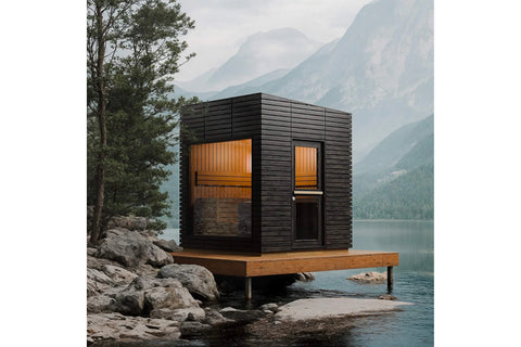 Modern black wooden sauna with orange interior, glass door and window, mounted on wooden deck over mountain lake