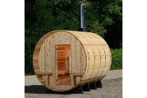 Barrel sauna made of light wood with horizontal planks, open wooden door visible, black metal chimney pipe extending from top
