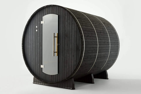 Black wood barrel sauna with glass door, brass handles, and metal bands, viewed on white background