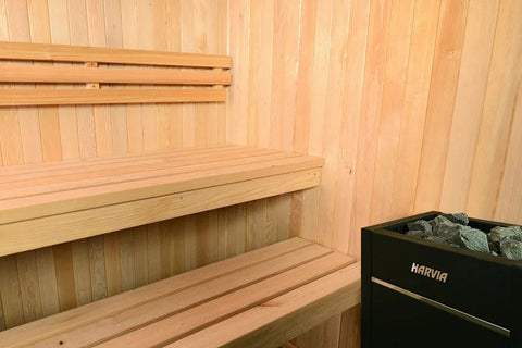 Light wood sauna with glass front doors, wooden bench seating, vertical paneling walls, and black heater unit on right side