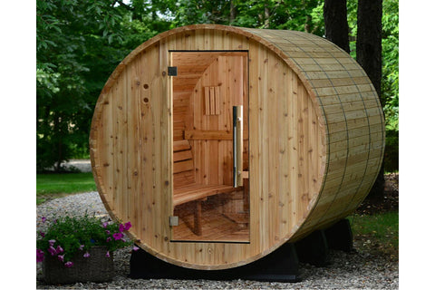 Cylindrical wood barrel sauna with light natural wood exterior, glass door showing interior benches and bucket, mounted on bl