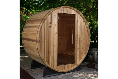Cylindrical wooden barrel sauna with glass door, cedar construction, and metal bands, on black support stand against white ba