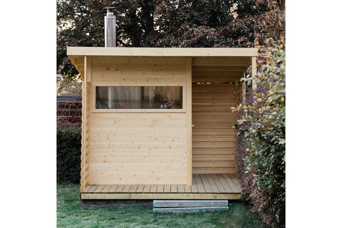 Natural pine wood sauna with large window, open right side, and metal chimney, positioned in backyard garden setting