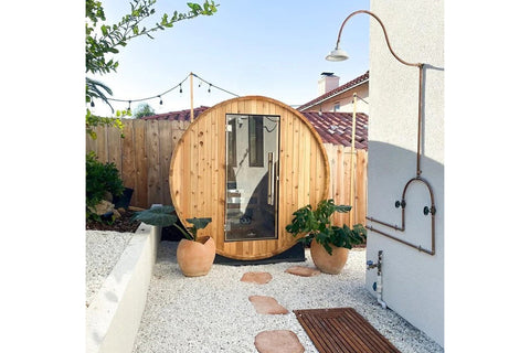 Almost Heaven Watoga barrel sauna with curved wooden exterior and glass door in backyard setting with potted plants