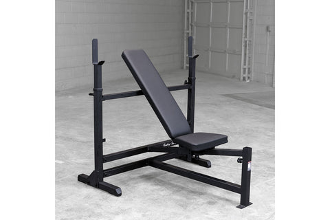 Body-Solid PowerCenter Combo Bench with black weight plates on barbell and leg attachment, gray steel frame on white backgrou