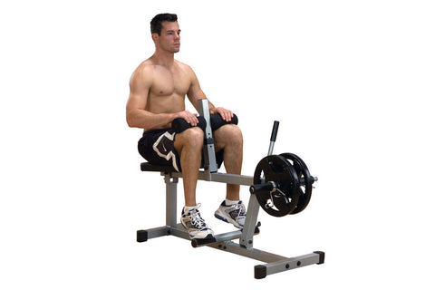 Seated calf raise machine with gray steel frame, black padded seat, cylindrical leg rest, and foot platform on white backgrou