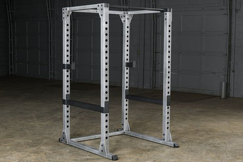 Body-Solid Pro Power Rack with gray and black steel frame, adjustable safety bars, and perforated upright posts on white back
