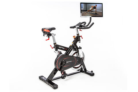 Black and red indoor training cycle with curved handlebars, padded seat, and stabilizer base on white background