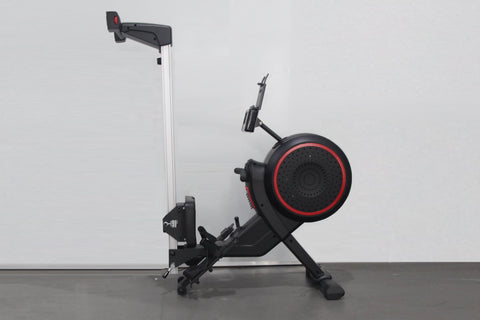 Black and red stationary rowing machine with aluminum rail, adjustable seat, foot pedals, and phone holder on white backgroun
