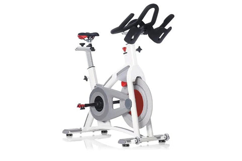 White and gray stationary exercise bike with red accents, black handlebars, and gray pedals on white background