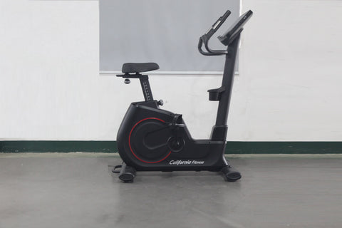 California Fitness U8 black upright exercise bike with red accents, digital display console, and padded seat on gray floor