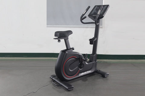 California Fitness U8 black upright exercise bike with red accents, digital display console, and padded seat on gray floor