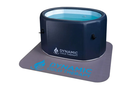 Dark navy inflatable cold plunge tub with turquoise water visible through clear top panel, sitting on gray mat with blue Dyna