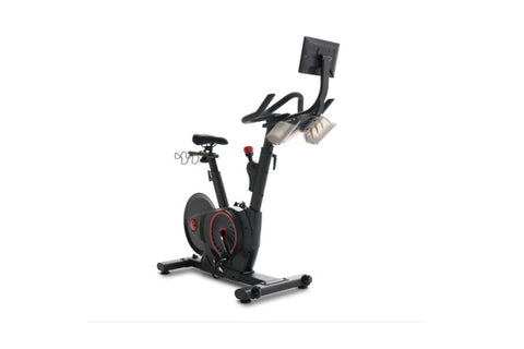 Black and red indoor stationary exercise bike with dual handlebar options and weighted flywheel on white background