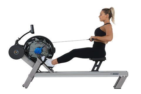 FluidRower E550 rowing machine with gray frame, black seat, blue resistance wheel, and digital monitor display on white backg