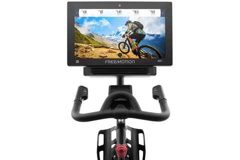 Freemotion CoachBike indoor exercise bike with black frame, blue accents, touchscreen display mounted on handlebar, and silve
