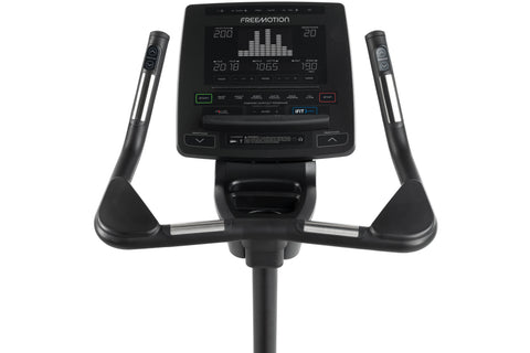 Black upright exercise bike with digital display console, padded seat, and stationary handlebars on white background