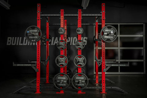 Hammer Strength red and black half combo power rack with loaded Olympic weight plates and barbell sleeves in gym setting