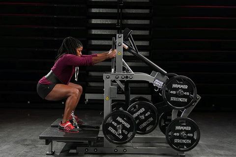 Black plate-loaded belt squat machine with dual foot platforms, weight horn attachments, and three vertical antenna posts on 