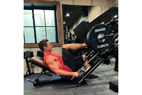Black Hammer Strength plate-loaded linear leg press with adjustable seat, numbered weight plates, and leg extension attachmen