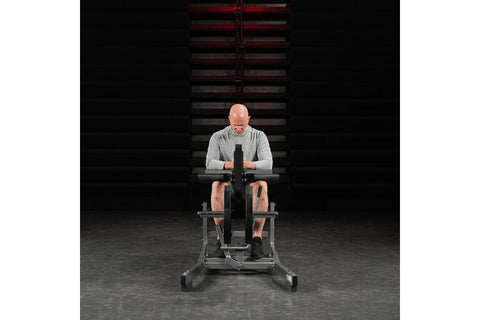 Black plate-loaded seated calf raise machine with padded seat and leg platform, chrome handles, on white background