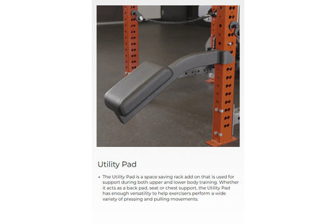 Gray and black curved utility pad attached to orange steel power rack frame in gym setting
