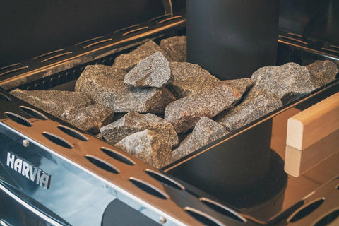 Harvia Pro 20 LS black and gray wood-burning sauna stove with gray rocks on top, visible flames in firebox, and built-in wate