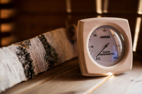 Harvia sauna thermometer with wooden frame, white dial face, and temperature scale from 0 to 120 degrees Celsius on white bac