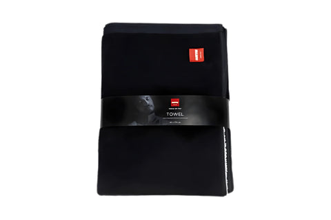 Black sauna towel with white "#healingwithheat" text, held by person at outdoor sauna deck with frozen lake and city skyline