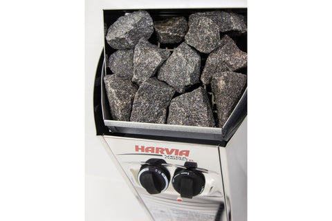 Harvia Vega Compact R electric sauna heater with stainless steel body, black control knobs, and gray stones in open top compa