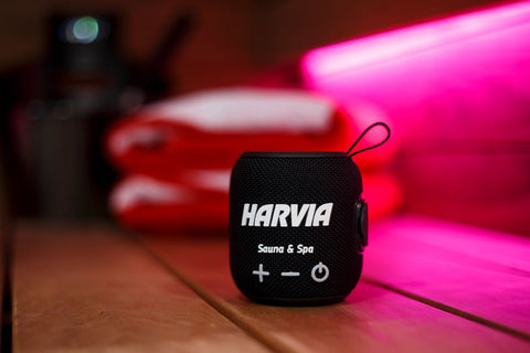 Harvia black water-resistant sauna speaker with metallic top, fabric body, control buttons, and carrying loop on white backgr