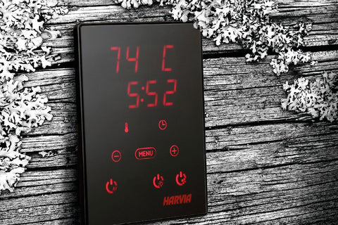 Black digital sauna control panel with red LED display showing temperature and time, mounted on wall with hand operating touc