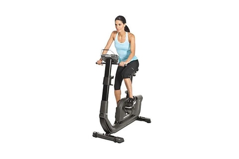 Black upright exercise bike with digital display console, handlebars, padded seat, and foot pedals on white background