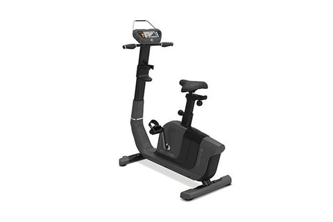 Black upright exercise bike with digital display console, handlebars, padded seat, and foot pedals on white background