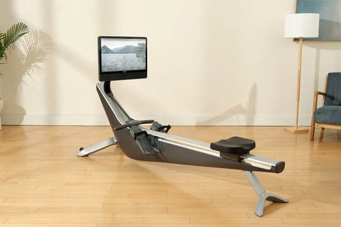 Hydrow Arc Rower with black seat and silver frame, mounted touchscreen displaying water rowing video, on wooden floor in home