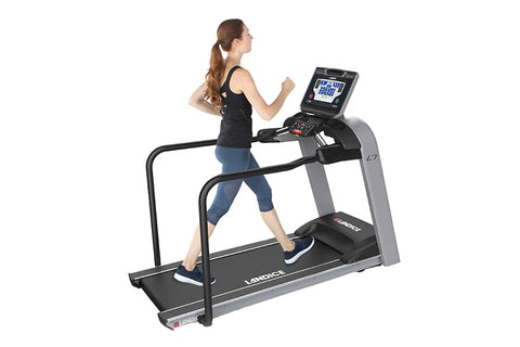 Woman running on black and gray Landice L7 treadmill with digital display console, worn by model on white background