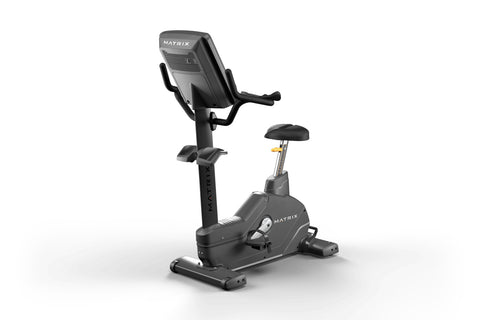 Matrix Endurance upright exercise bike with black frame, digital display console, dual handles, and black padded seat on whit